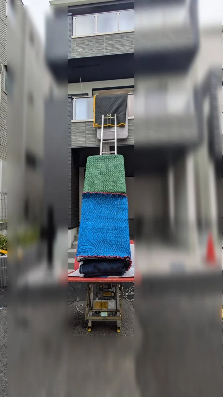 住宅の外から電動はしごを使い、上階の窓付近へ大型家電を搬入する作業