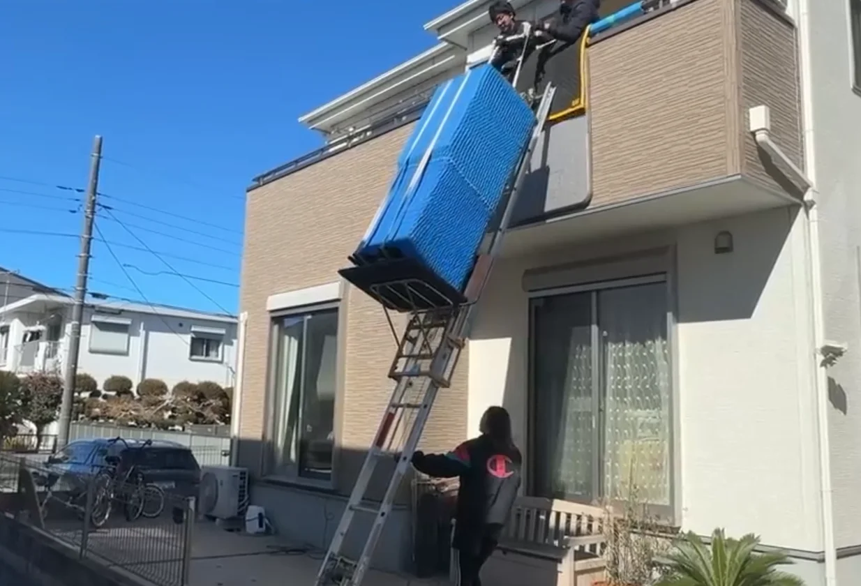 外壁沿いに電動はしごを設置し二階へ大型家具を搬入するスタッフたち