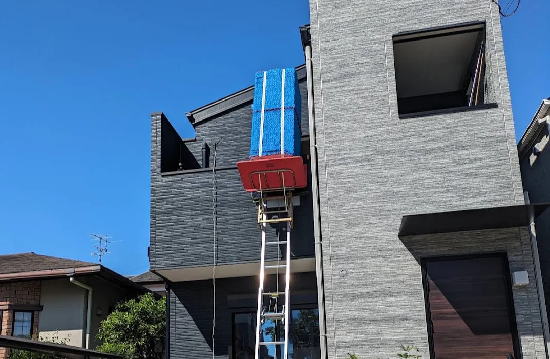電動はしごで建物の窓から大型寝具を吊り上げて搬入する作業