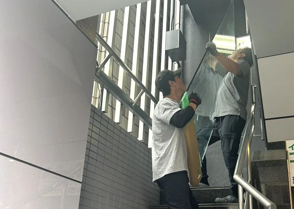 階段の踊り場でガラス製の家具を二人がかりで慎重に運び上げる作業員