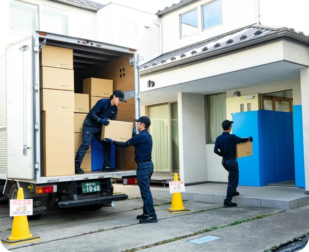 引越しトラックの荷台から段ボールを受け渡しし、住宅へ搬入する作業員たち