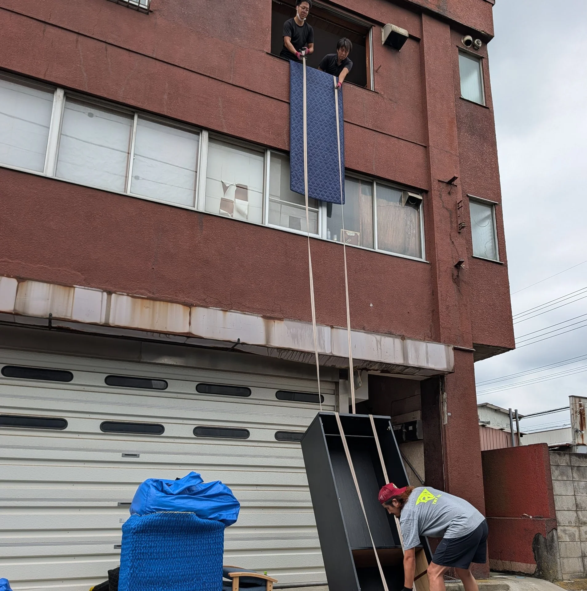 建物上階の窓からロープで大型家具を吊り下ろし、地上の作業員が受け取る搬出作業